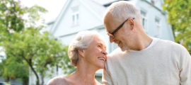 elderly couple standing smiling in front of home